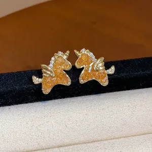 Primer plano de pendientes de unicornio dorados con cristal naranja y circonitas blancas
