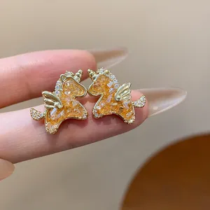 Vista macro de pendientes de unicornio dorados con incrustaciones de vidrio ámbar