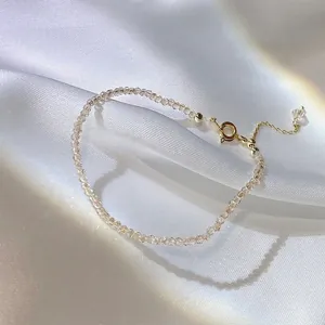 Nahaufnahme eines zarten Armbands aus Champagner-Kristallperlen auf weißem Seidenstoff