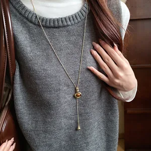 Close-up of a retro oval resin pendant necklace worn with a grey knit vest outfit