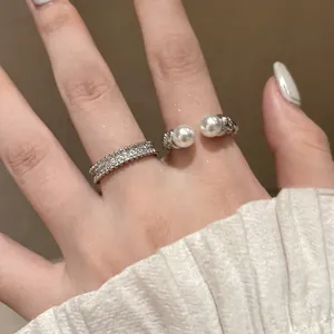 Elegant detail shot of a pavé zircon band and open-ended pearl ring on a finger.