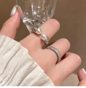 Detail shot of a minimalist open pearl ring and sparkling zircon band on a finger