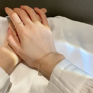 Detailaufnahme von minimalistischen champagnerfarbenen Kristallarmbändern und Ringen.