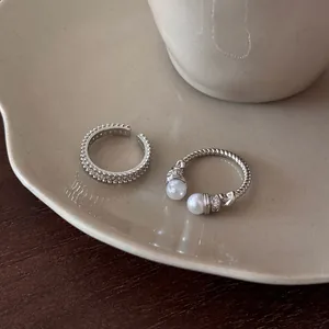 Close-up of silver-toned zircon and pearl textured adjustable open rings on a ceramic plate.