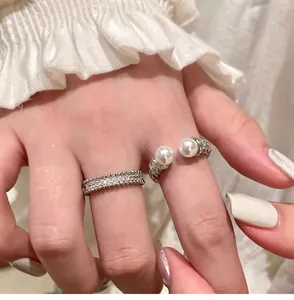 Macro detail of elegant zircon pavé band and twin pearl open ring on model hand.