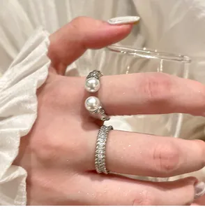 Close-up of elegant silver-colored open ring with pearls and a shimmering zircon band ring.