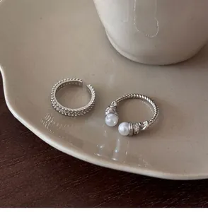 Detailed macro view of silver zircon paved band and twisted pearl open ring on ceramic plate