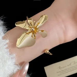 Close-up detail showing a vintage-style gold metal flower cuff bracelet worn on a wrist