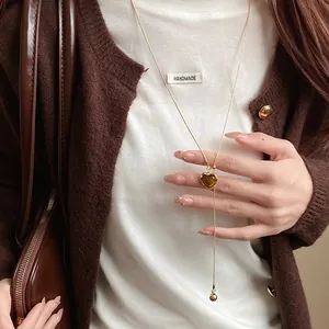 Detail view of a retro heart-shaped resin pendant necklace worn with a brown cardigan