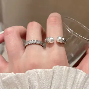 Close-up of minimalist zircon band and elegant open pearl ring set on finger