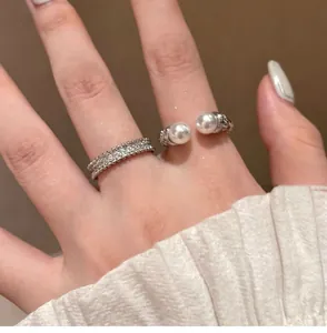 Close-up detail of silver-toned zircon band and pearl open ring on finger