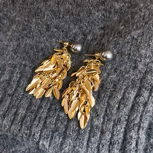 Detailed view of gold leaf tassel earrings with elegant grey pearls on knit fabric.