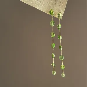 Close-up of elegant long drop earrings with translucent green crystals and gold chains