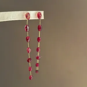 Close-up of retro red crystal drop earrings with long gold chain and organic red beads.