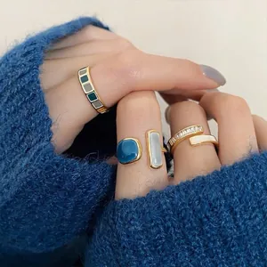 Vista detallada de anillos geométricos de esmalte en una mano con jersey de punto azul suave.