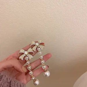 Close-up detail of elegant gold tassel earrings with rhinestone bowknots and pearls.