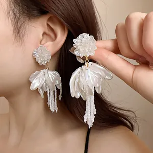 Detailed view of elegant white flower petal earrings with beaded tassels on a model ear.