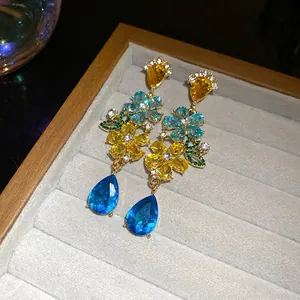 Elegantes pendientes de flores doradas con colgantes de gota azules y cristales