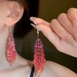 Close-up view of elegant gradient pink rhinestone feather tassel earrings on a model.