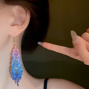 Close-up of gradient blue and pink rhinestone feather tassel earrings worn by a model.