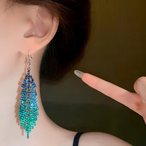 Detailed view of long gradient blue and green rhinestone tassel earrings on model