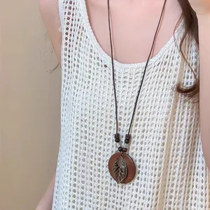 Gros plan d'un collier ethnique long avec disque en bois et pendentif feuille en métal