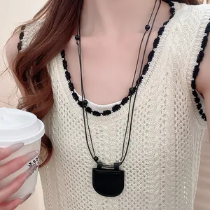 Gros plan d'un long collier noir de style Zen avec un petit pendentif en forme de sac