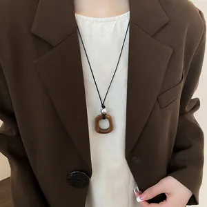 Long collier de style Zen avec pendentif carré marron porté sur un blazer marron.