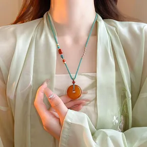 Détail d'un collier Zen néo-chinois avec un pendentif donut en ambre sur un cordon vert