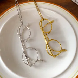 Detail of silver and gold metal glasses pendant necklaces on a white ceramic plate.
