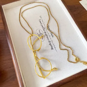 Detailed view of a gold-finish eyeglass pendant necklace on a wooden jewelry tray.