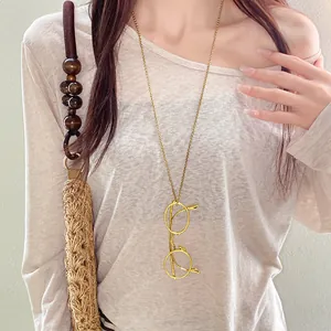 Close-up of a stylish gold metal eyeglass pendant on a long necklace chain shown on a model.