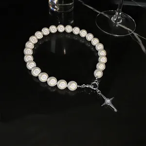 Collier de perles élégant avec pendentif étoile argenté minimaliste sur une surface sombre.