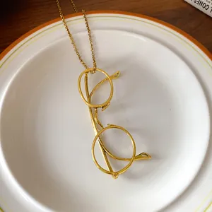 Close-up detail of a vintage gold glasses-shaped pendant necklace on a white plate