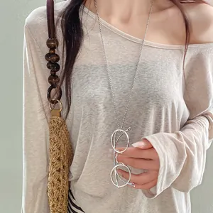 Detail shot of a stylish silver metal glasses pendant necklace on a beige textured shirt.