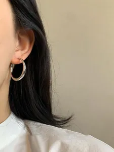 Dettaglio ravvicinato di un orecchino a cerchio geometrico in argento lucido su una modella