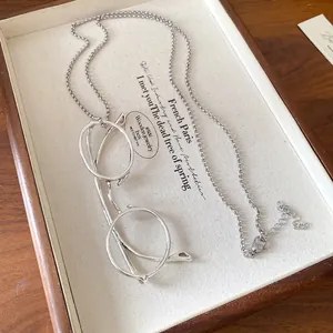 Detail of silver glasses pendant necklace displayed on a vintage wooden jewelry tray.