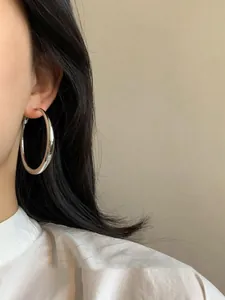 Primo piano di grandi orecchini a cerchio in argento lucido minimalisti indossati da una modella