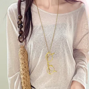 Macro detail view of a vintage gold glasses pendant necklace on a soft beige knit top