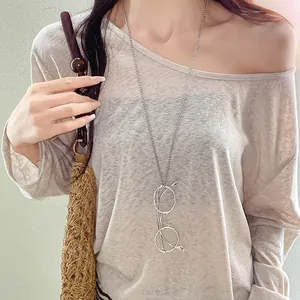 Detail of a minimalist silver metal necklace with a unique glasses-shaped pendant on a model.
