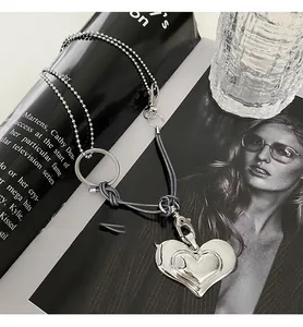 Primer plano de un collar vintage con corazón, cordón gris y cadena de bolas.