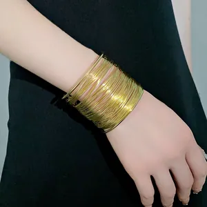 Close-up of a multi-layer gold wire cuff bracelet worn on a wrist over black fabric.