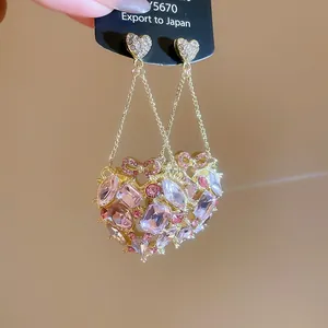 Close-up of sparkling gold heart tassel earrings with pink crystals and butterfly bows.