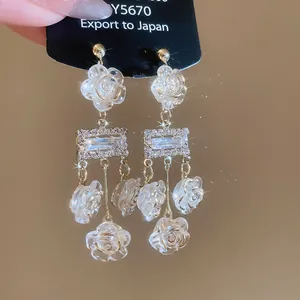 Detail showing elegant silver needle dangle earrings with white roses and diamond sparkles.