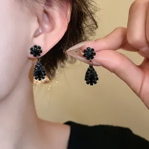 Nahaufnahme eleganter schwarzer Strass-Ohrringe in Tropfenform am Ohr und in der Hand gehalten