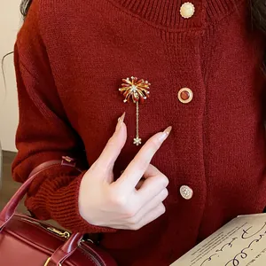 Close-up of elegant firework brooch with dangling snowflake charm on red cardigan