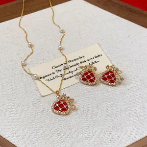 Close-up view of a gold-plated red fortune bag necklace and earring jewelry set with white pearls