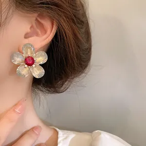 Elegante pendiente de flor con pétalos claros y una gema roja brillante en la oreja.