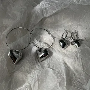 Close-up of small and large silver heart hoop earrings on textured white paper background.