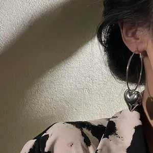 Detailed close-up of minimalist silver hoop earrings with heart pendant on model